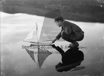 Boy crouching with model yacht